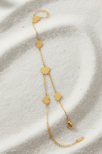 Gold bracelet with heart-shaped charms on a textured beige surface