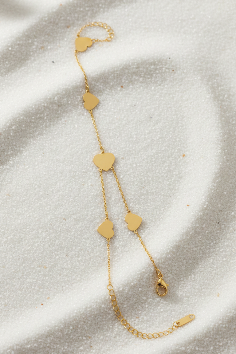 Gold bracelet with heart-shaped charms on a textured beige surface