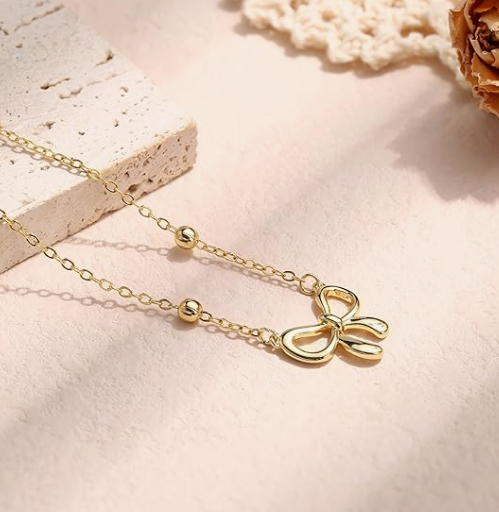 Gold necklace with a bow pendant on a soft pink background