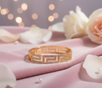 Gold bracelet on a pink fabric background with blurred lights and flowers.