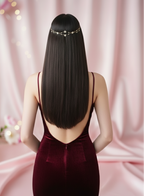 Woman in a burgundy dress with a decorative hair accessory against a pink curtain background