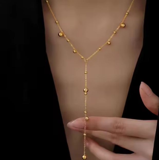 Gold body chain worn on a person's arm with a black background