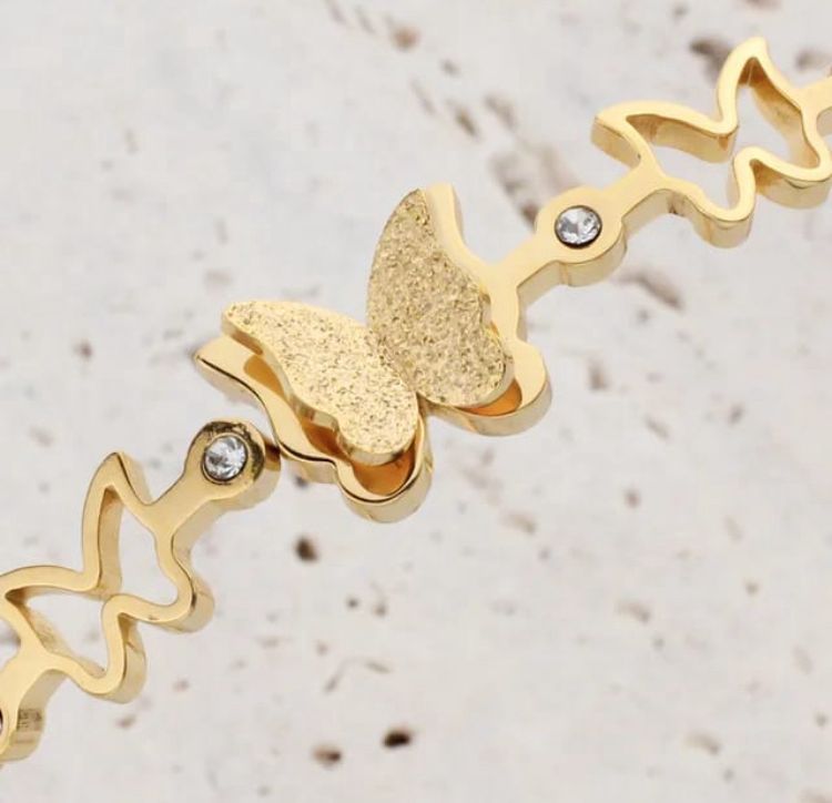 Dainty Gold Butterfly Cuff Bracelet with Crystal Accents - ORYX TREND BraceletsAn elegant gold-tone bangle bracelet featuring a central, intricately textured butterfly charm. The rest of the cuff is adorned with delicate cutout butterfly shapes, interspersed with small, sparkling crystal accents. This piece uses a durable, hinged clasp for secure and comfortable wear. It beautifully symbolizes transformation and grace, making it a perfect statement piece or a thoughtful gift.Default Title#
