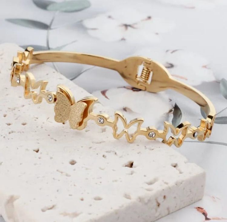Dainty Gold Butterfly Cuff Bracelet with Crystal Accents - ORYX TREND BraceletsAn elegant gold-tone bangle bracelet featuring a central, intricately textured butterfly charm. The rest of the cuff is adorned with delicate cutout butterfly shapes, interspersed with small, sparkling crystal accents. This piece uses a durable, hinged clasp for secure and comfortable wear. It beautifully symbolizes transformation and grace, making it a perfect statement piece or a thoughtful gift.Default Title#