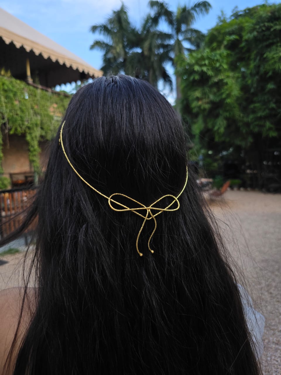 Person wearing a gold hair accessory with a bow design outdoors.