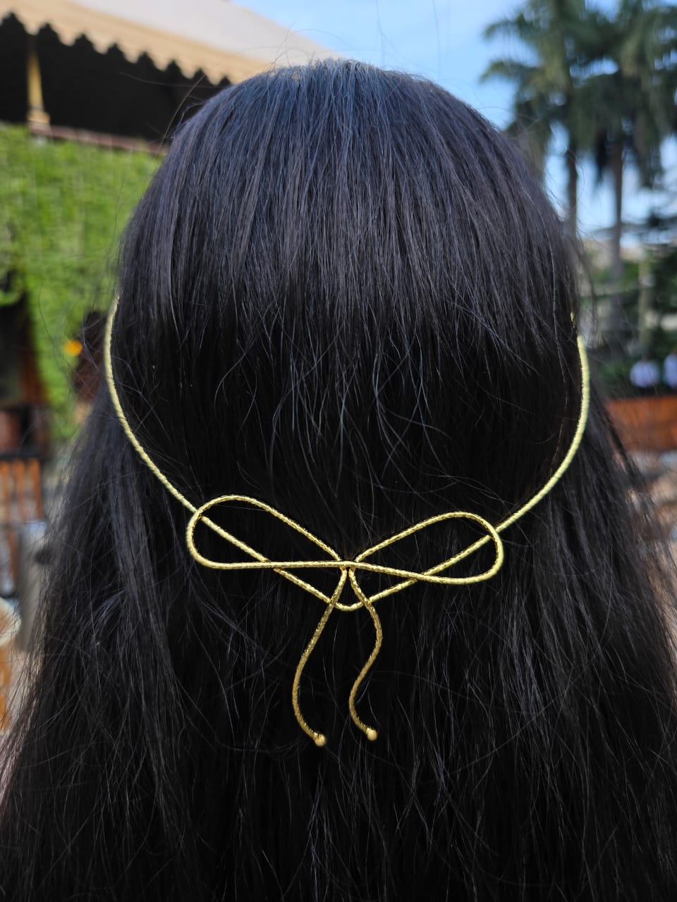 Gold hair accessory shaped like a bow on black hair with a blurred outdoor background