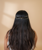 Person with long dark hair wearing a delicate gold headband in a home setting with plants.