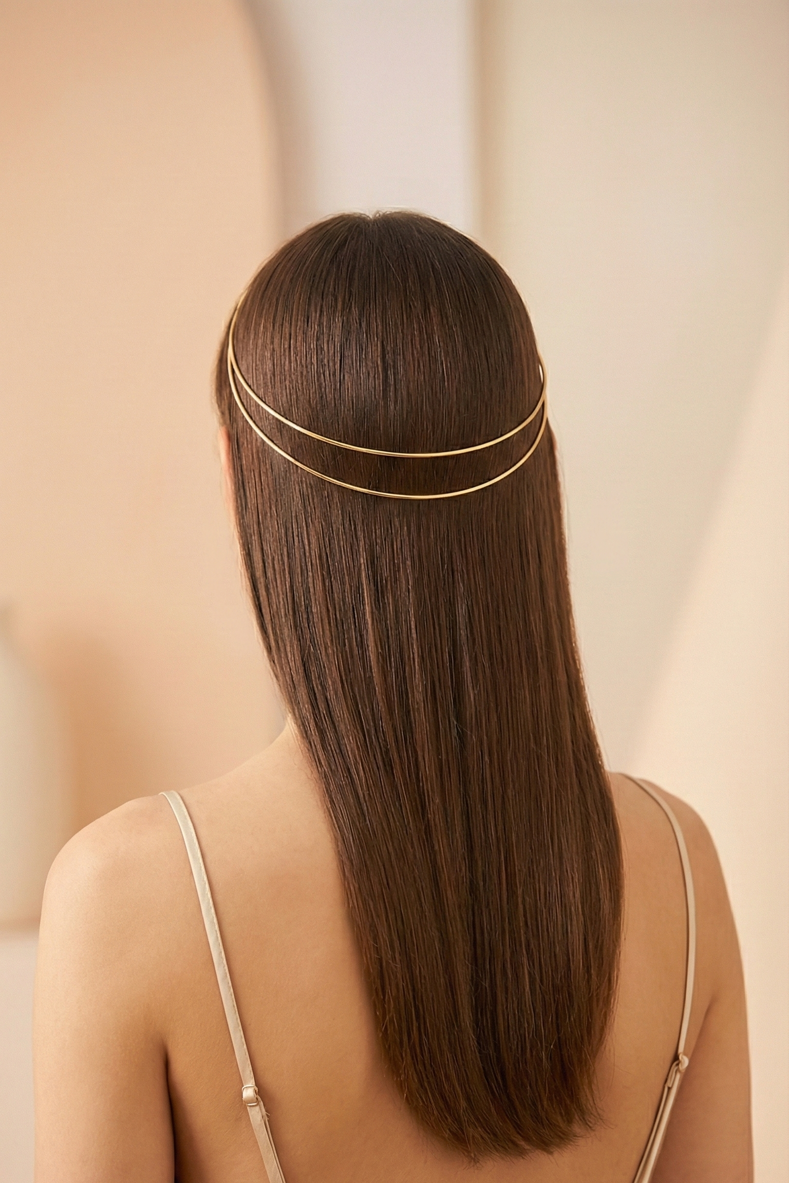 Woman with long straight hair wearing a thin gold headband against a beige background