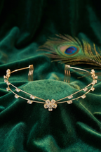 Gold headband with floral designs on a green velvet surface with a peacock feather in the background.