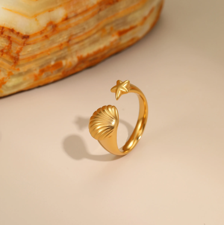Gold ring with shell and star design on a beige background