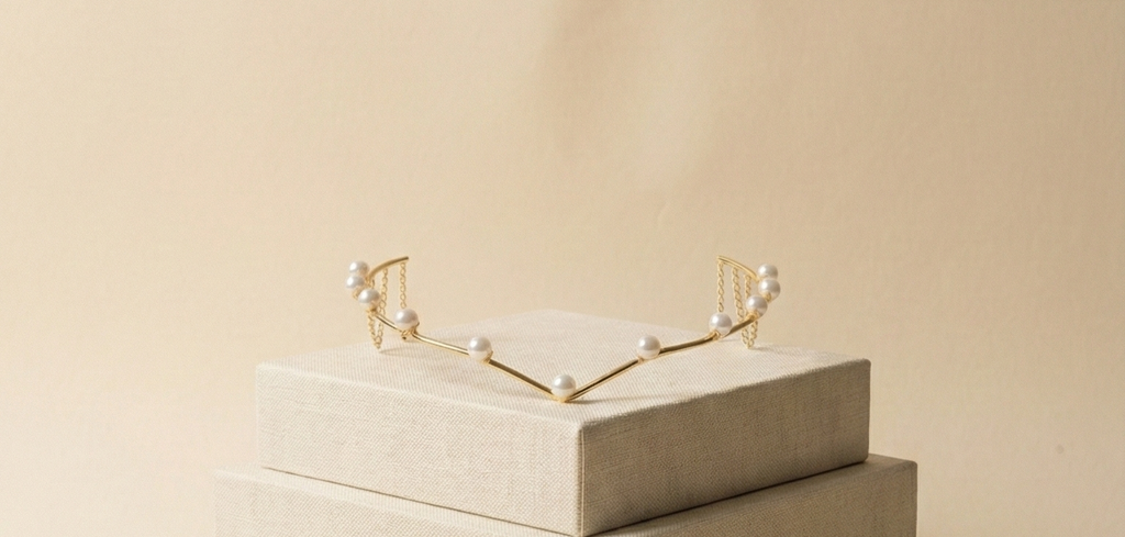 Gold headband with pearls on a beige box against a beige background