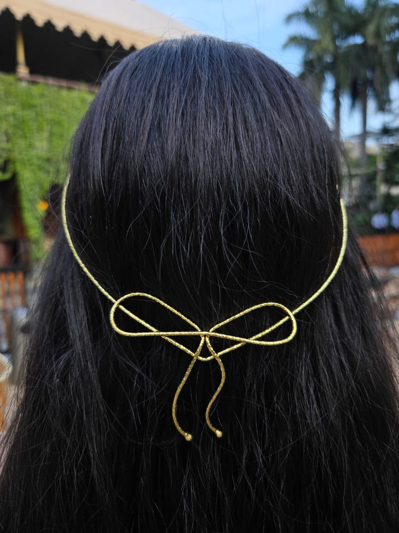 Gold hair accessory shaped like a bow on black hair with a blurred outdoor background