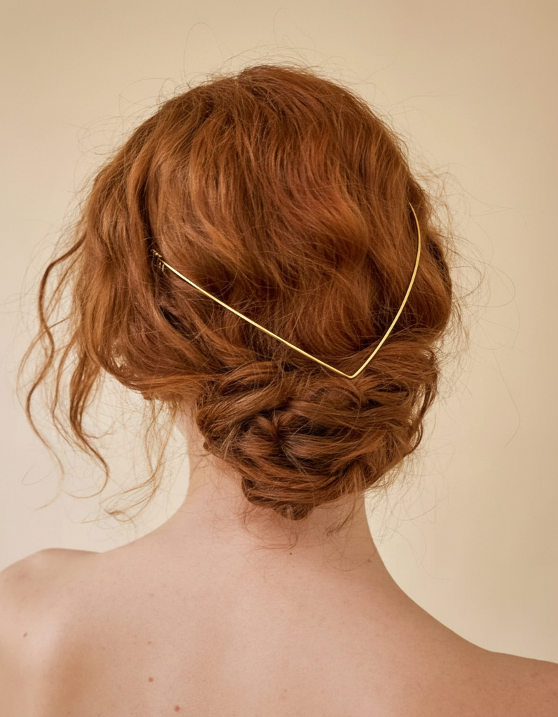 Person with red hair styled in an updo wearing a gold hair accessory against a beige background