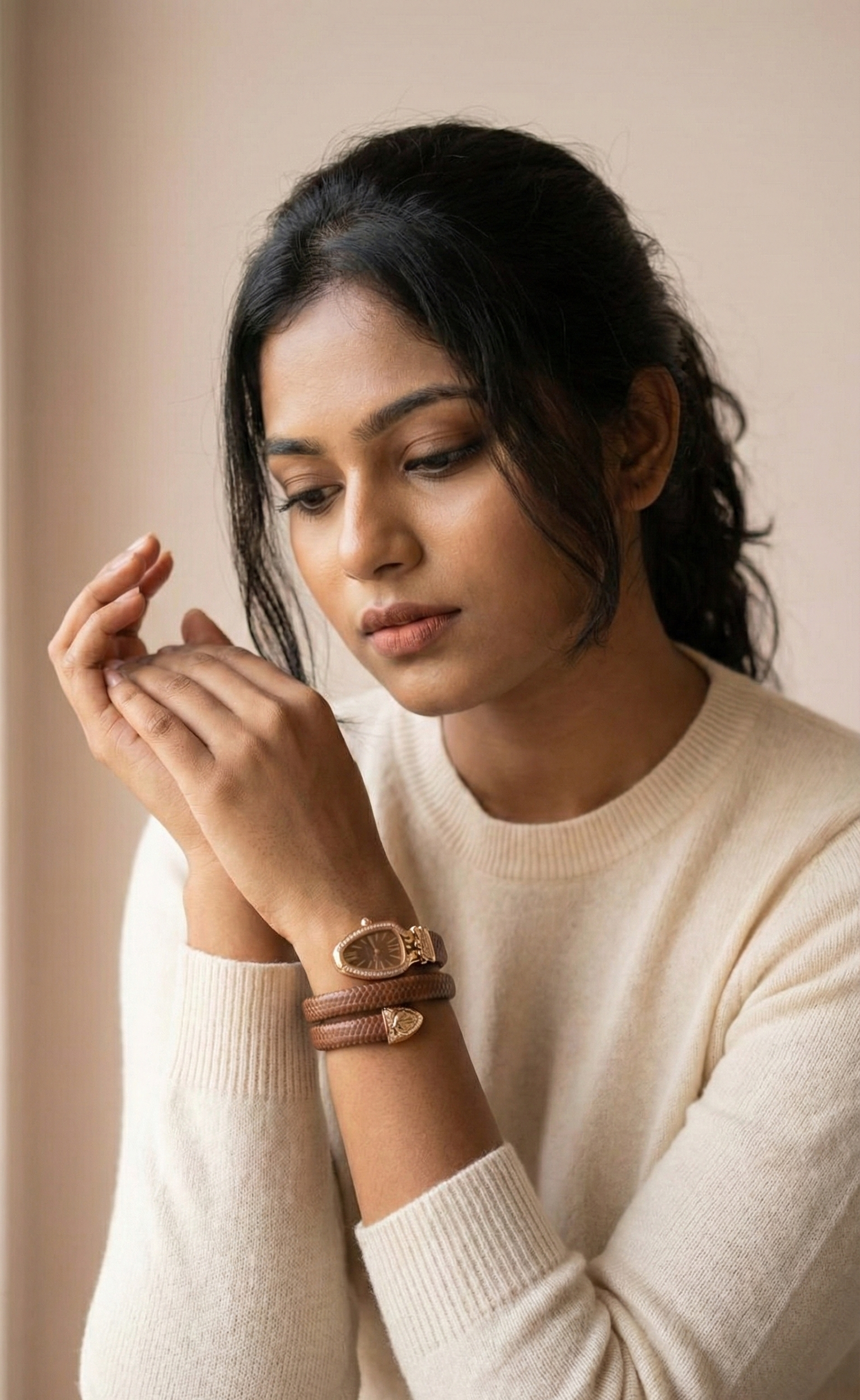 Woman wearing a white sweater and multiple bracelets on a neutral background