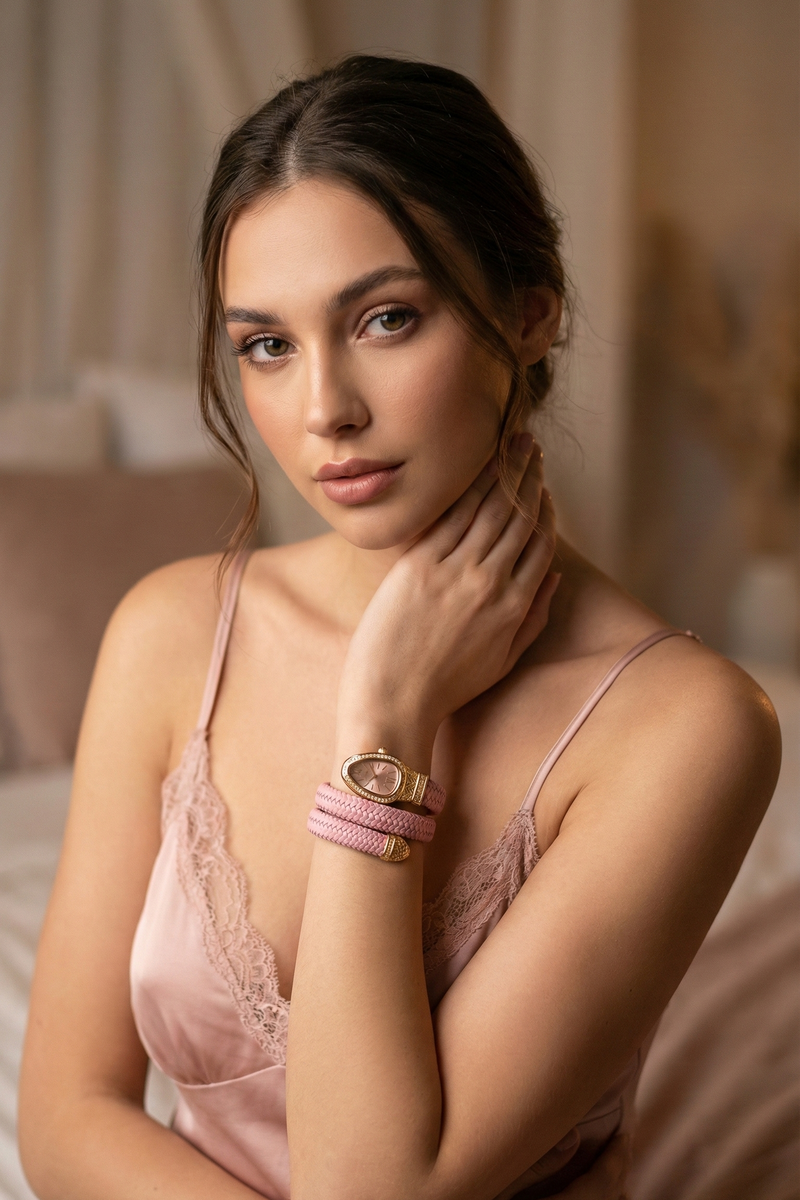 Woman wearing a pink lace nightgown with jewelry, sitting on a bed.