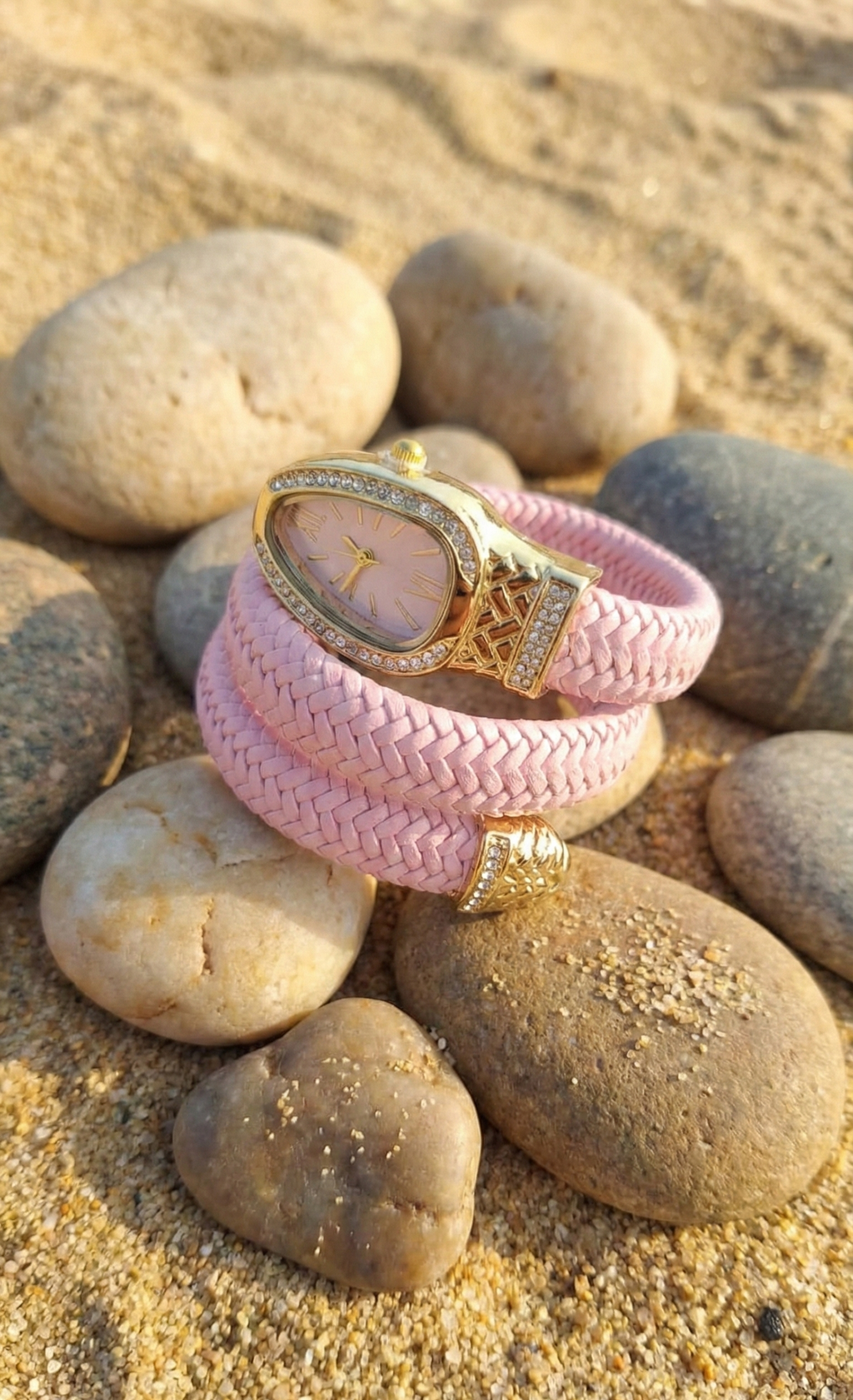 Pink braided bracelet with gold watch face on pebbles