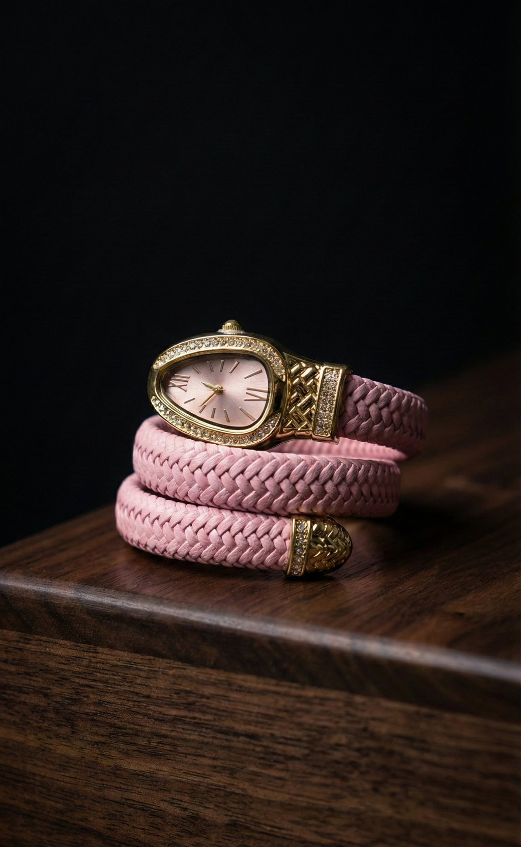 Pink braided bracelet with gold clasp on a dark wooden surface