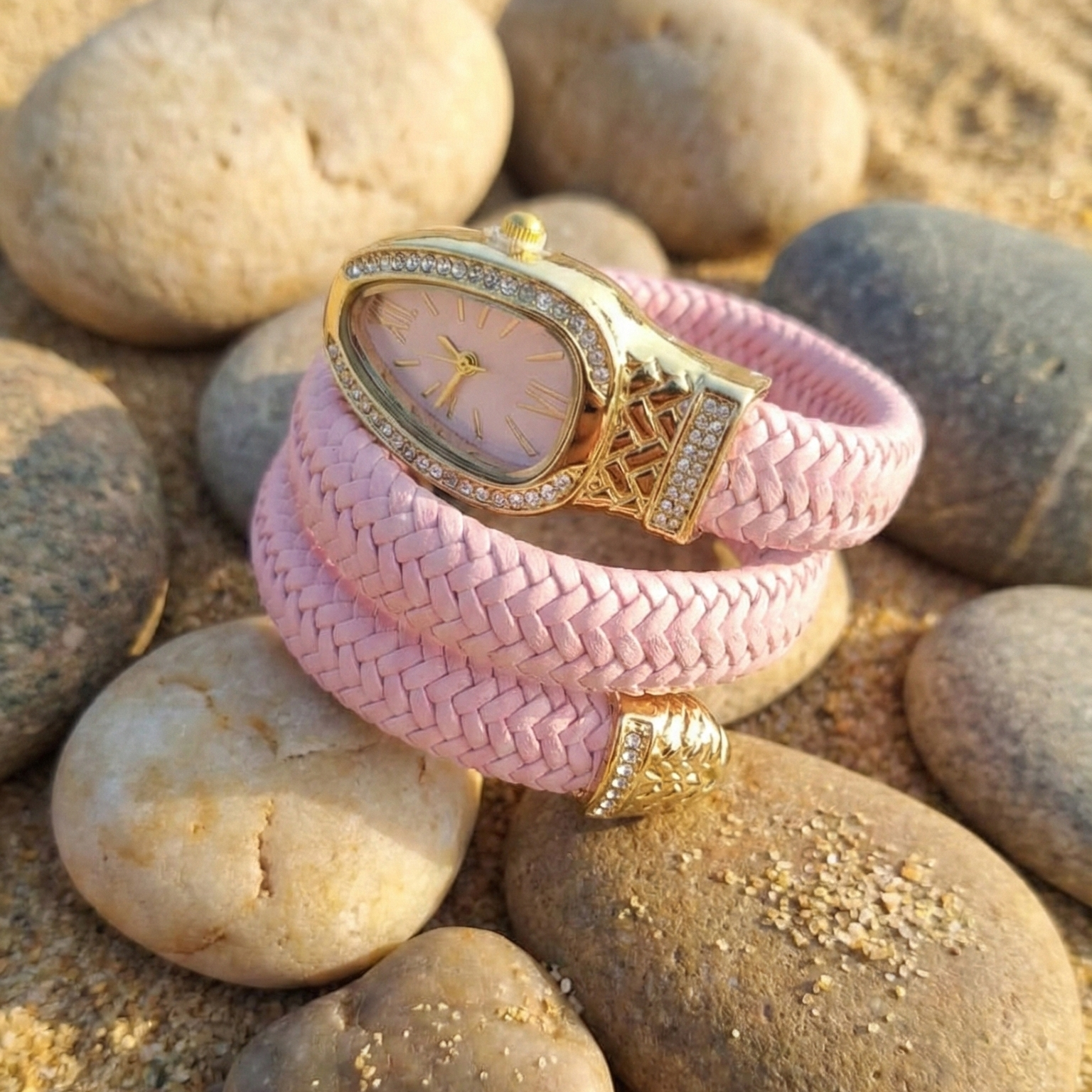 Pink braided bracelet with gold watch face on pebbles