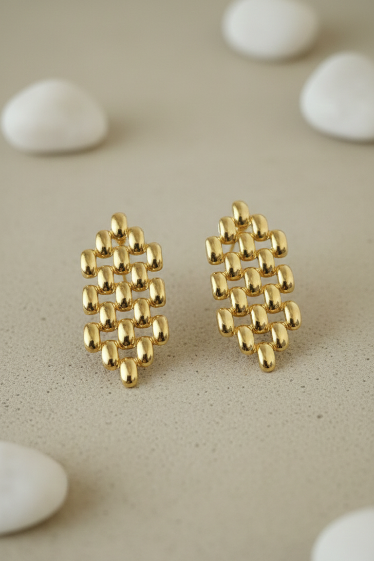 Gold lattice earrings on a beige surface with white stones
