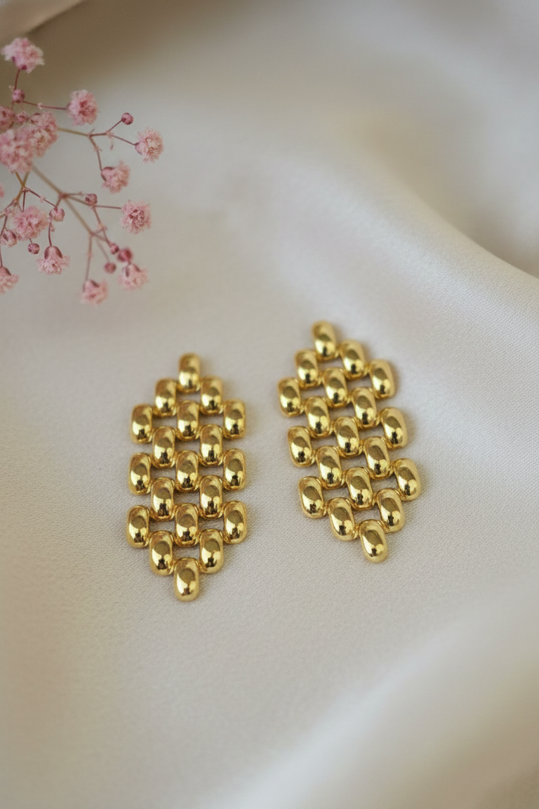 Gold earrings on a light pink fabric background with pink flowers.