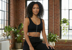 Woman in black athletic wear sitting on a stool in a room with large windows and plants.