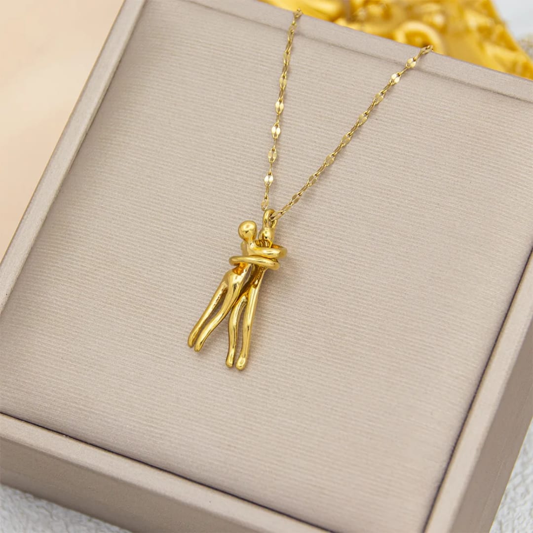 The Embrace Necklace: Gold-Tone Hug Pendant - ORYX TREND NecklaceA beautifully artistic necklace featuring a minimalist pendant design that captures the tender moment of an intimate embrace. The gold-tone pendant depicts two stylized figures locked in a hug, symbolizing love, connection, comfort, and friendship. Suspended from a delicate gold-toned chain (perhaps a flat link or paperclip style), this unique piece makes a deeply personal and meaningful gift for a loved one.Default Title#