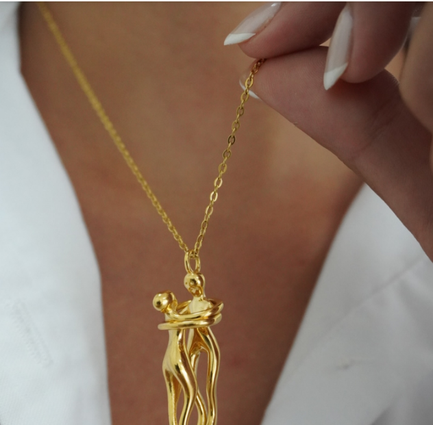 The Embrace Necklace: Gold-Tone Hug Pendant - ORYX TREND NecklaceA beautifully artistic necklace featuring a minimalist pendant design that captures the tender moment of an intimate embrace. The gold-tone pendant depicts two stylized figures locked in a hug, symbolizing love, connection, comfort, and friendship. Suspended from a delicate gold-toned chain (perhaps a flat link or paperclip style), this unique piece makes a deeply personal and meaningful gift for a loved one.Default Title#