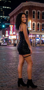 Woman in a black sequin dress standing on a city street at night.