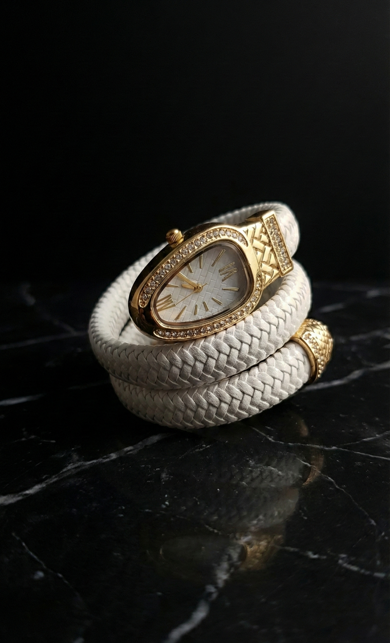 White braided leather bracelet with gold watch face on a dark reflective surface
