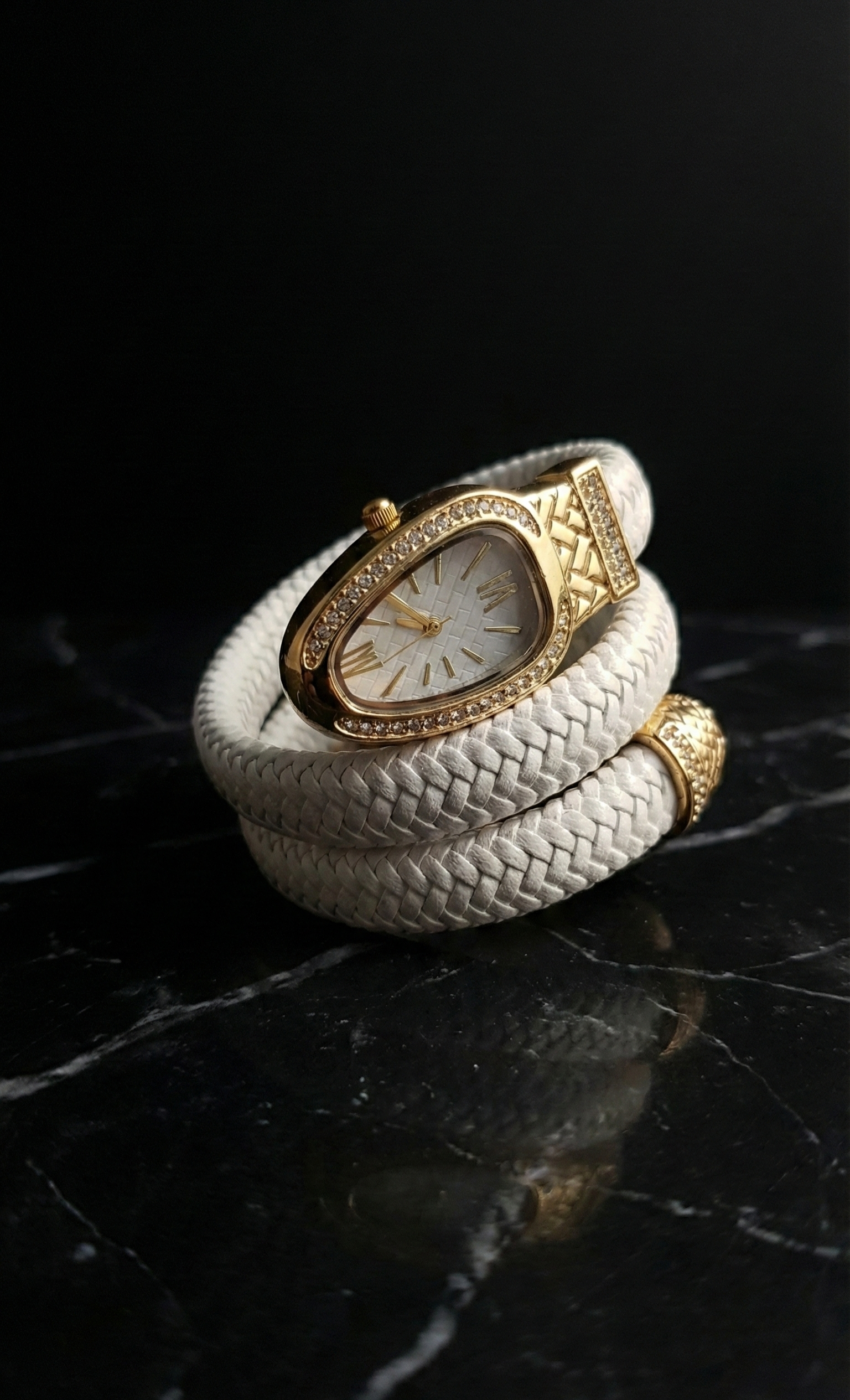 White braided leather bracelet with gold watch face on a dark reflective surface