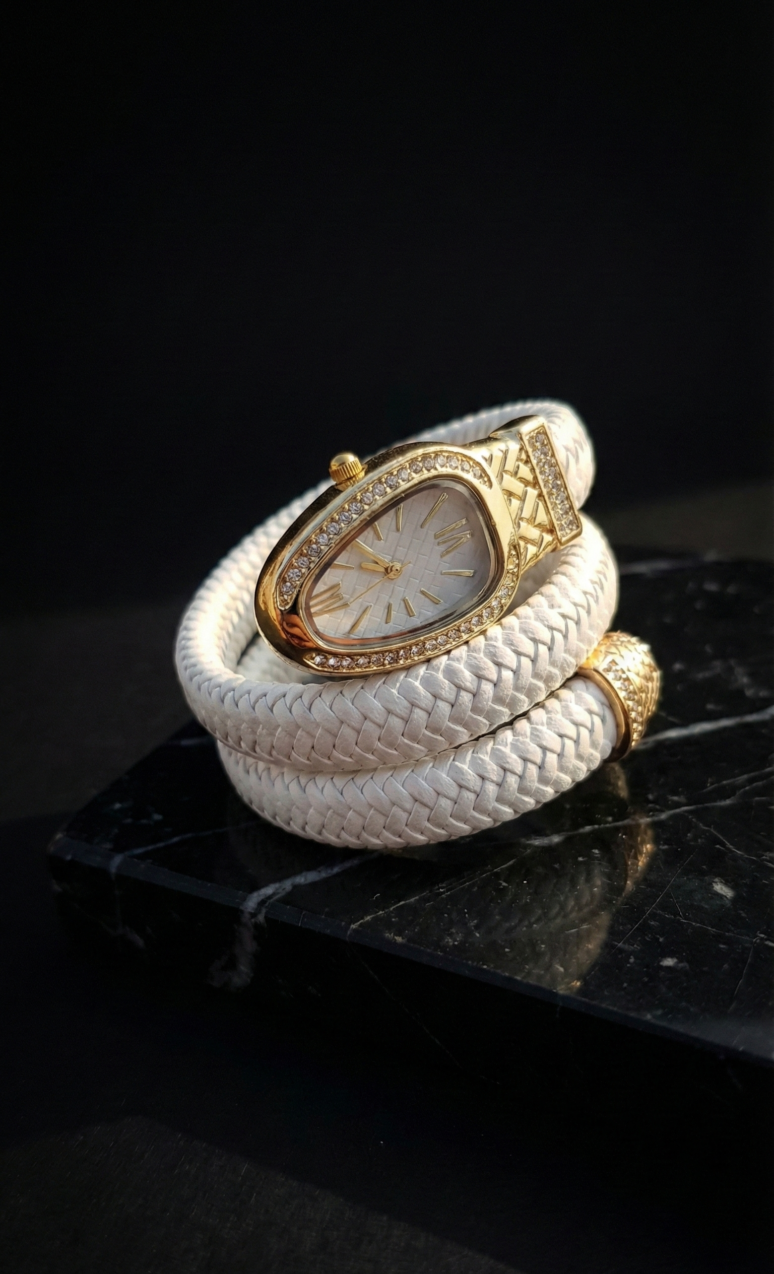 Gold watch with a white woven strap on a dark surface